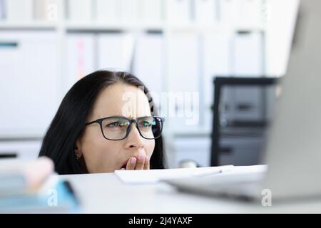 Scioccata donna emotiva guarda da sotto il tavolo al computer Foto Stock