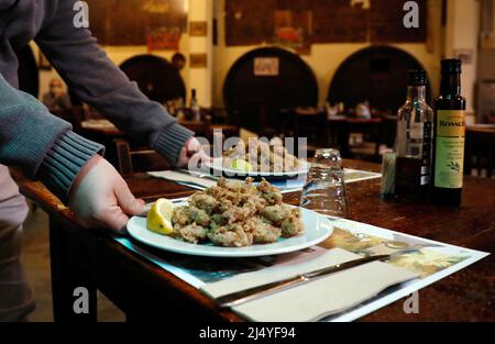 Palma, Spagna. 18th Apr 2022. Toni, cameriere del ristorante 'Sa Pressa' con cucina tipica maiorchina, serve una tapa con calamari fritti l'ultimo giorno delle vacanze pasquali. Credit: Clara Margais/dpa/Alamy Live News Foto Stock