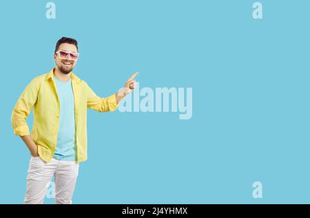 Uomo felice in abiti estivi casual e occhiali da sole che punta a copiare spazio su sfondo blu Foto Stock