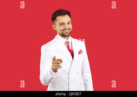 Felice uomo giovane sicuro in abito bianco sorridente e puntando il dito indice alla fotocamera Foto Stock