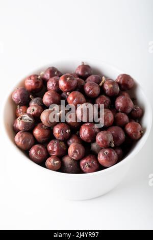 Bacche di ginepro su sfondo bianco. Juniper semi in una ciotola bianca isolato. Foto Stock