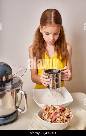 Una ragazza adolescente cuoca una torta fatta in casa, una torta con mele in cucina. Mescola gli ingredienti per la torta in un mixer elettrico. Primo piano. Foto Stock