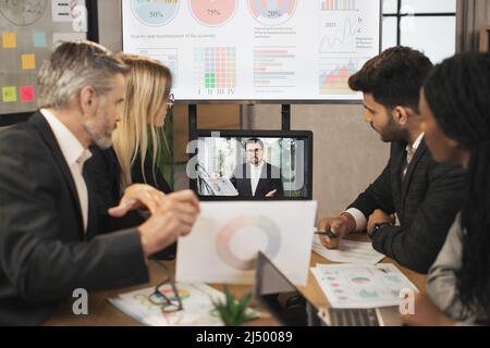 Concetto di riunione elettronica. Diversi gruppi di uomini d'affari multirazziali nella sala conferenze ascoltano le istruzioni dei loro colleghi d'affari durante una videoconferenza da un computer portatile. Foto Stock