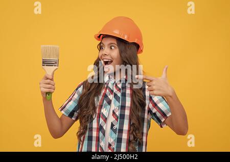 stupito teen ragazza che punta il dito sulla pittura pennello. bambino pittore in casco. Foto Stock