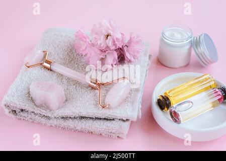 Set di cosmetici naturali biologici spa con fiori sakura. Rullo facciale, fiori di ciliegia, crema cosmetica e olio su sfondo rosa. Cura della pelle, bellezza tre Foto Stock