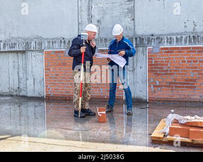 Kemerovo, Russia - 24 giugno 2021. Due ingegneri in cappelli duri stanno studiando il piano di struttura mentre si trovano su una superficie di calcestruzzo bagnata, nelle mani di un solo uomo Foto Stock