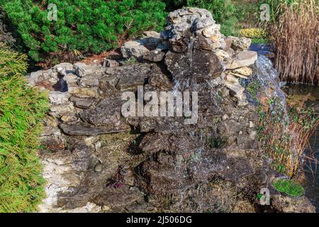 Cascata d'acqua decorativa nel parco . Spruzzi d'acqua su pietre Foto Stock