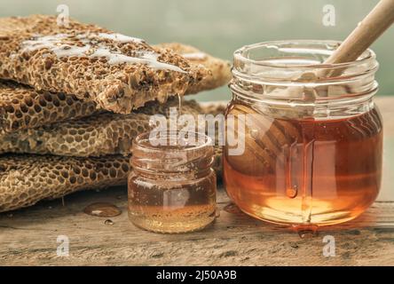 Primo piano di miele delizioso che gocciola da nido d'ape freschi su vaso di vetro con bastone di legno del divipper del miele su vecchio tavolo di legno. Sano biologico natura hon Foto Stock