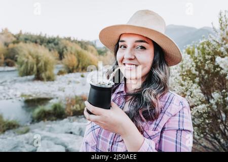 Giovane donna caucasica con un cappello, bevendo compagno in uno spazio naturale con un umore autunnale. Foto Stock