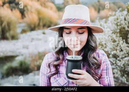 Giovane donna caucasica con un cappello, bevendo compagno in uno spazio naturale con un'atmosfera estiva. Foto Stock