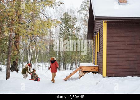 Il giovane uomo afro-americano in inverno tira la slitta con suo figlio durante una passeggiata nella gelida giornata invernale presso la loro casa di campagna Foto Stock