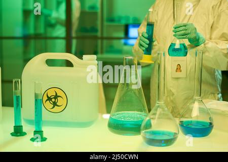 Medico contemporaneo in tute e guanti che contengono due provette con sostanza tossica liquida blu mentre si trova sul posto di lavoro in laboratorio Foto Stock