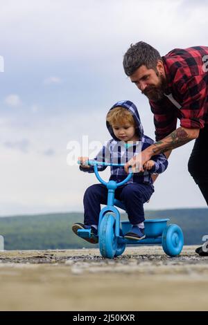 Padre che insegna a suo figlio di andare in bicicletta. Il ragazzino impara a guidare una bicicletta con il suo papà. Papà insegnando a figlio di andare in bicicletta. Foto Stock