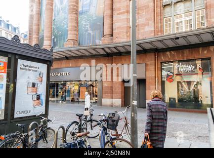 Strasburgo, Francia - Apr 11, 2022: Vista posteriore della donna anziana che cammina vicino alle biciclette parcheggiate al grande magazzino Galeries Lafayette di mattina presto Foto Stock