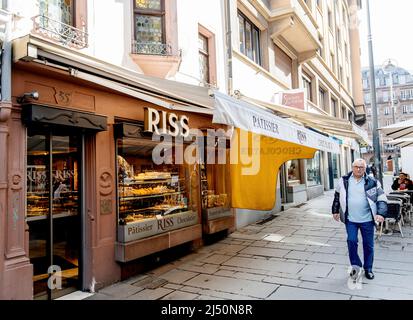 Strasburgo, Francia - Apr 11, 2022: Uomo anziano a piedi vicino alla tradizionale pasticceria Riss negozio di panetteria nel centro di Strasburgo con persone in background bere caffè in terrazza - 35 Rue du Vingt-Deux Novembre Foto Stock