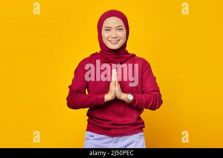 La giovane donna asiatica che indossa il foulard dà il benvenuto con il grande sorriso sul suo volto isolato su sfondo giallo Foto Stock