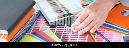 Donna designer guarda attraverso lente d'ingrandimento alla tavolozza di colori con diverse sfumature di colori Foto Stock