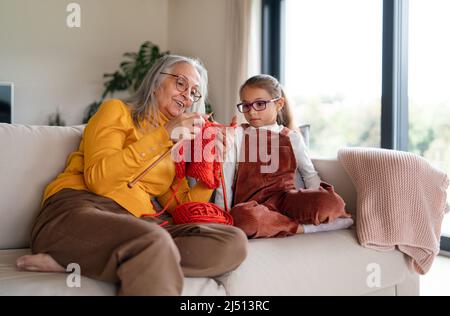 Bambina seduta sul divano con la nonna e imparare a lavorare a maglia in casa. Foto Stock