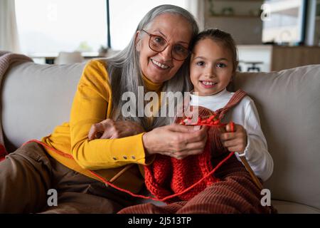 Bambina seduta sul divano con la nonna e imparare a lavorare a maglia in casa. Foto Stock