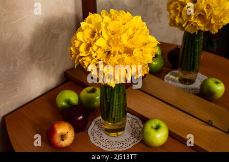 Un grosso bouquet di naffodils gialli in vaso su un tavolo di legno, con mele Foto Stock