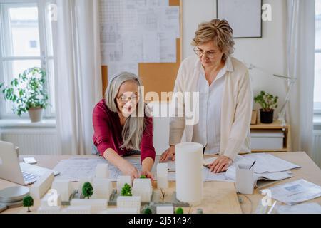 Le donne mature eco architetti con modello di moderni bulidings e progetti che lavorano insieme in ufficio. Foto Stock