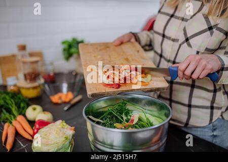 Donna gettando talee vegetali in un secchio di composto in cucina. Foto Stock