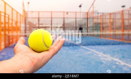 Il formatore insegna il paddel a studente maschile sul campo da tennis all'aperto. Uomo che gioca il padel in un campo di erba blu all'aperto dietro la rete Foto Stock