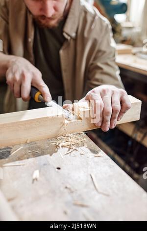 Alto angolo medio primo piano dell'uomo che lavora in carpenteria tagliando mortasa in legno con scalpello Foto Stock