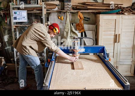 Carpentiere professionale che regola la fresatrice CNC per realizzare dettagli in legno in officina Foto Stock