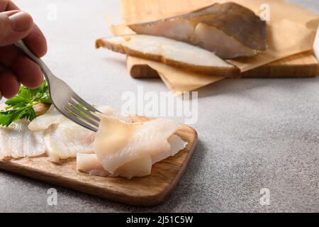 Fette di halibut affumicate su sfondo grigio. Uomo che mangia pesce prelibato. Primo piano. Foto Stock