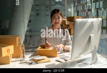 Giovane imprenditore asiatico di piccole dimensioni che lavora in ufficio a casa, prendendo nota degli ordini di acquisto. Online marketing packaging delivery, avvio PMI imprenditore Foto Stock