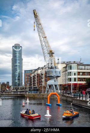 I bambini guidano le barche giocattolo intorno ad un vecchio molo disutilizzato nella zona commerciale di Gunwharf Quays a Portsmouth, Hampshire, Regno Unito. Foto Stock