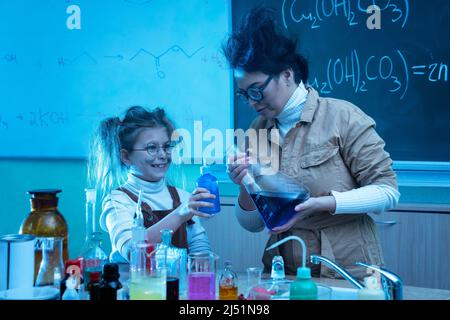 Divertente insegnante e bambina durante la lezione di chimica miscelazione di sostanze chimiche in un laboratorio Foto Stock