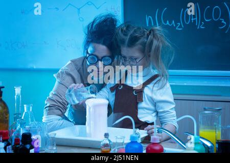 Divertente insegnante e bambina durante la lezione di chimica miscelazione di sostanze chimiche in un laboratorio Foto Stock