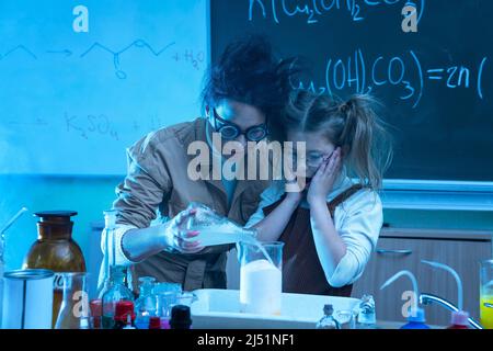 Divertente insegnante e bambina durante la lezione di chimica miscelazione di sostanze chimiche in un laboratorio Foto Stock