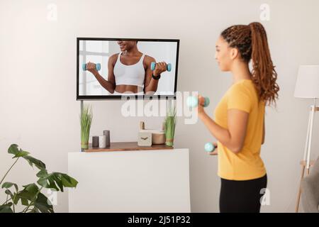 Sport Lady esercizio Holding Dumbbells guardare l'allenamento in televisione al chiuso Foto Stock