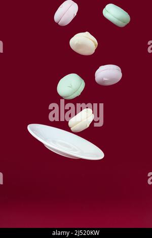 Piattino di porcellana che vola con marshmallows su sfondo rosso, concetto di dolce dessert. Concetto di gravità Foto Stock