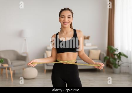 African Woman misura vita con nastro che mostra perdita di peso interno Foto Stock