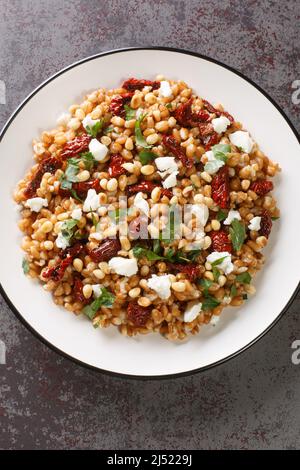 Insalata dietetica a base di farro, feta, pomodori secchi e pinoli da vicino in un piatto sul tavolo. Vista dall'alto verticale Foto Stock