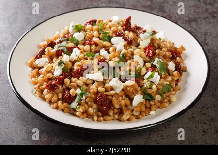 Farro di cereali a grani interi cotto come insalata con verdure e formaggio feta primo piano in un piatto sul tavolo. Orizzontale Foto Stock