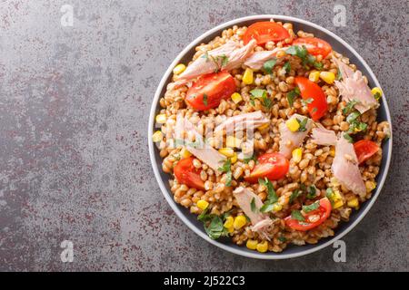 Insalata dietetica fatta in casa a base di farro, tonno, mais, pomodori e erbe da vicino in un piatto sul tavolo. Vista dall'alto orizzontale Foto Stock