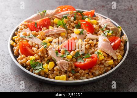 Insalata dietetica fatta in casa a base di farro, tonno, mais, pomodori ed erbe da vicino in un piatto sul tavolo. Orizzontale Foto Stock