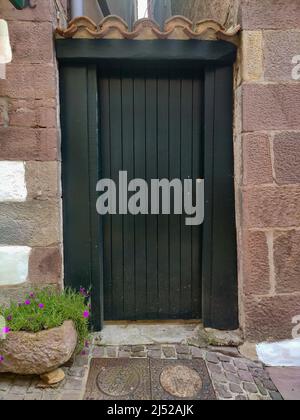 Porta in legno verde in una strada francese circondata da un muro roccioso e con pietre. Fotografia verticale. Foto Stock