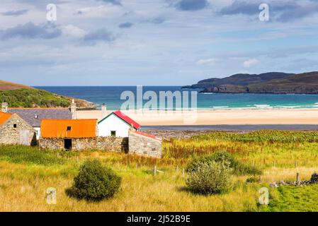 Un piccolo gruppo di vecchi edifici agricoli si affaccia su una grande spiaggia deserta, sabbiosa e mare turchese brillante a Torrisdale Bay, in una giornata di sole. Foto Stock