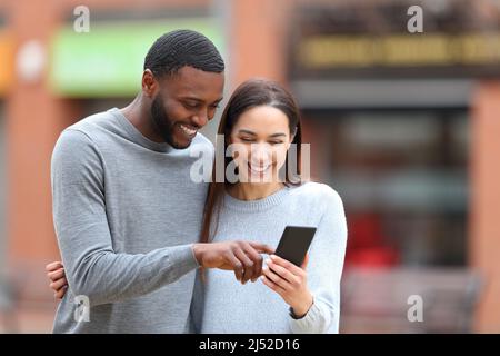 Felice coppia interrazziale controllo cellulare ridendo all'aperto per strada Foto Stock