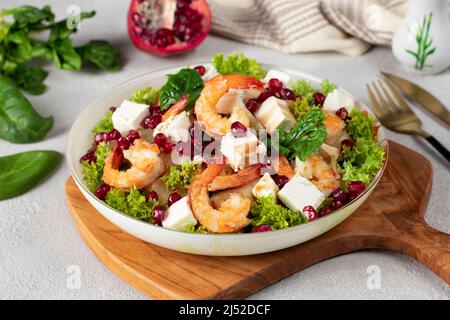 Insalata con gamberetti, ananas, feta e semi di melograno in un piatto su foglie di lattuga verde, su tavola di legno Foto Stock