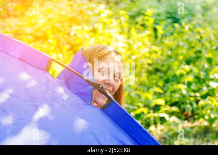 La ragazza teen defocus guarda fuori dalla tenda finestra in campeggio. Sfondo verde natura. Foresta o giardino. Felice, riposa, viaggia. SunFlare. Sfocato. Di Foto Stock