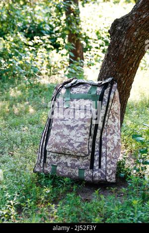 Zaino militare defocus. Borsa esercito su sfondo verde erba vicino albero. Materiale di nastro per camouflage militare su zaino dell'esercito britannico, zaino Foto Stock