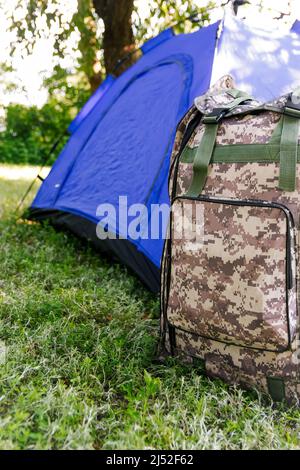 Sfocatura blu tenda turistica aperta in piedi su sfondo verde natura. Zaino militare. Concetto di turismo. Vacanze estive nella foresta, campeggio. Stile di vita Foto Stock