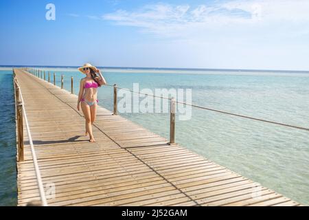 giovane donna sorridente in cappello di paglia che cammina sul pontile di legno Foto Stock